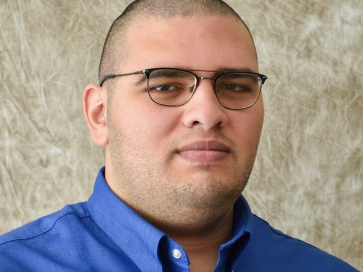 Man in a blue collared shirt against a beige textured background.