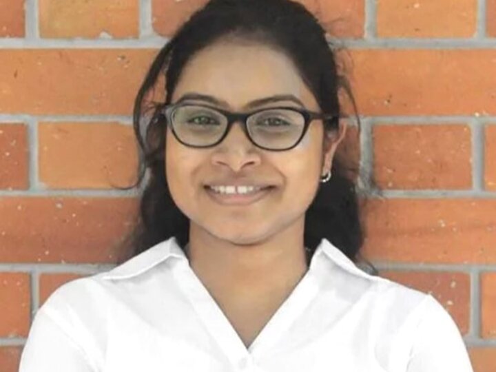 Person in a white shirt standing against a brick wall.