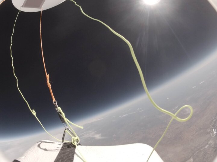 Earth's horizon from a high-altitude balloon, with cords and bright sunlight in view.