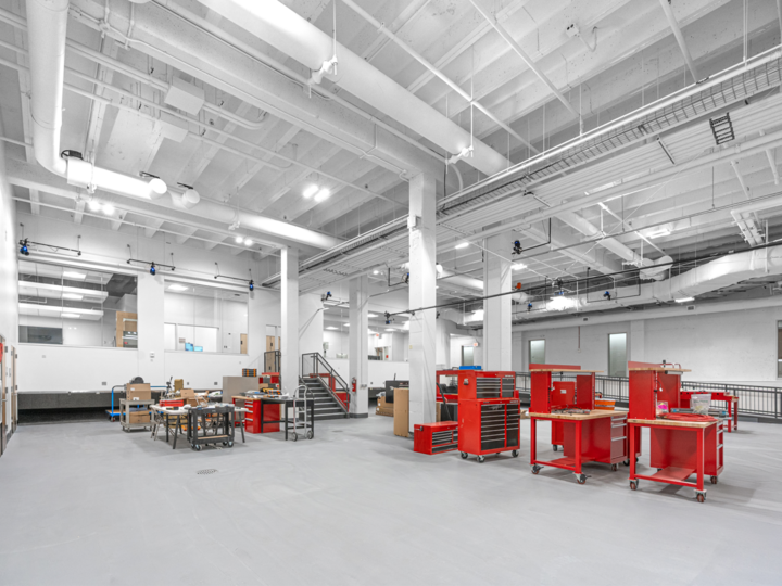 Spacious industrial workshop with red tool stations, white walls, and exposed pipes on the ceiling.