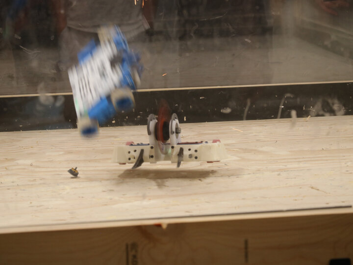 Robots in a battle arena, one flipping another with spinning wheels.