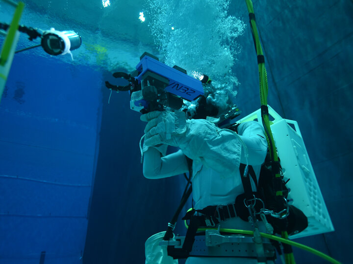 Astronaut training underwater in a neutral buoyancy pool, holding a tool and surrounded by bubbles.