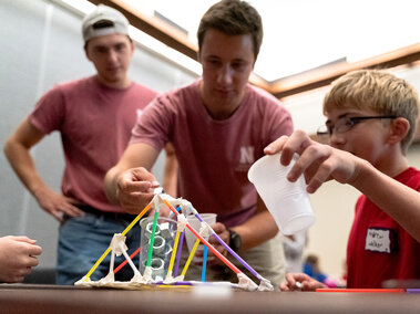 Two adults and a child building a colorful straw structure during a hands-on activity.