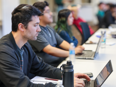 Students sitting at a long table with their computers.