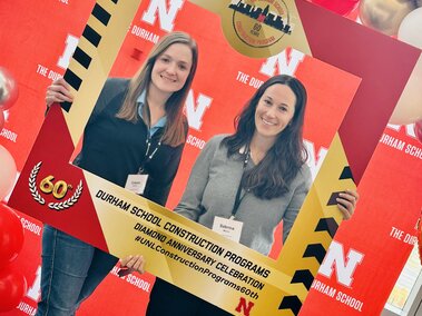 2 women pose with a square wooden frame