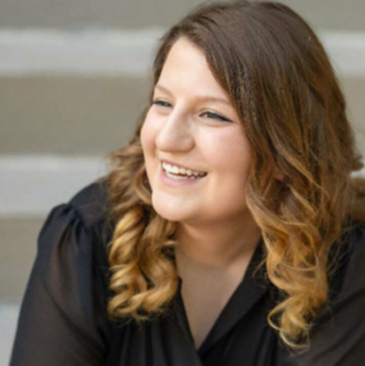 Woman with curled blonde hair wearing a black blouse, seated in front of grey steps.