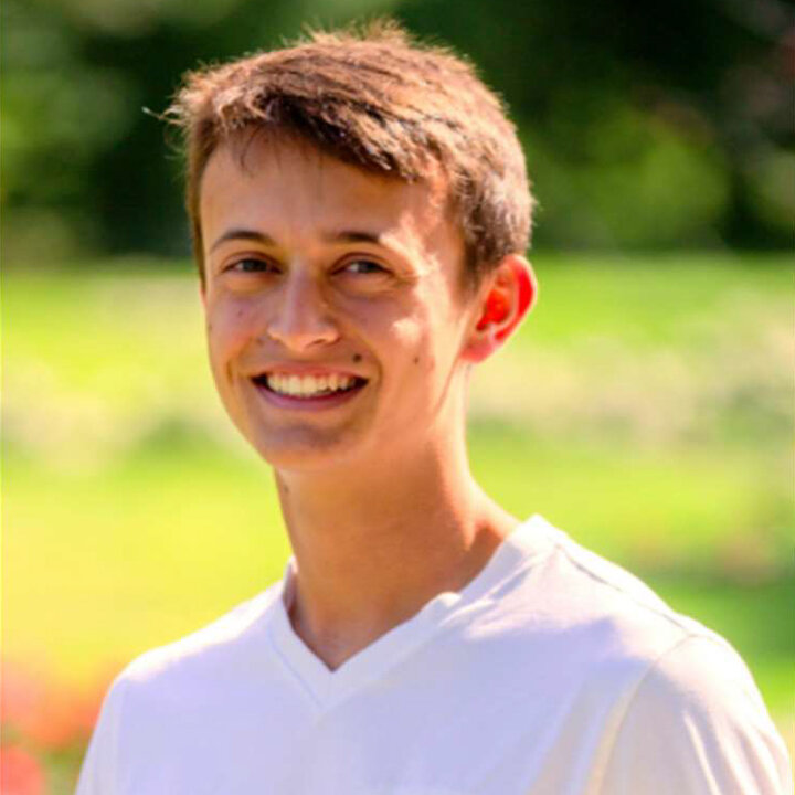 Person in a white shirt outdoors with blurry green background.