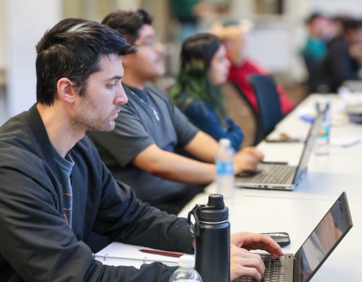 Students sitting at a long table with their computers.