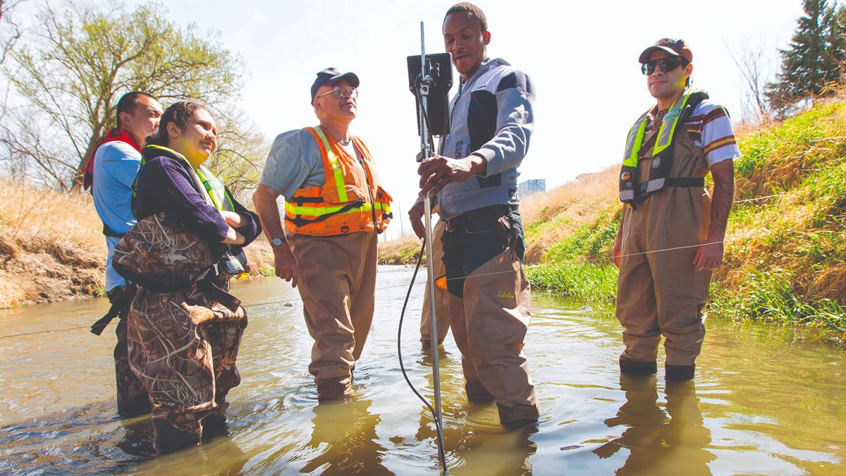 Five people standing knee-deep in a river with water-testing equipment