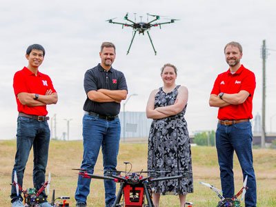 Three men and a woman stand by several drones