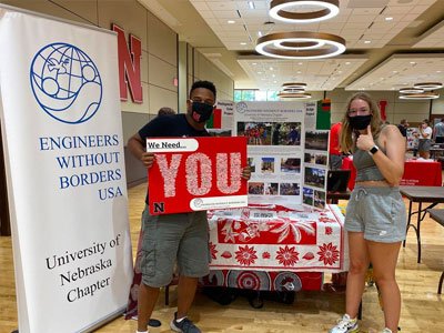 Two members of EWB stand by a table holding signs
