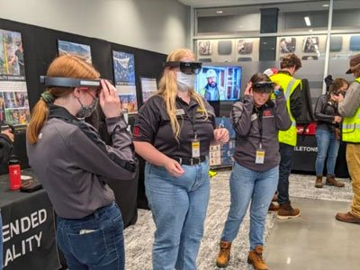 Three women students try on virtual reality goggles during an industry tour.