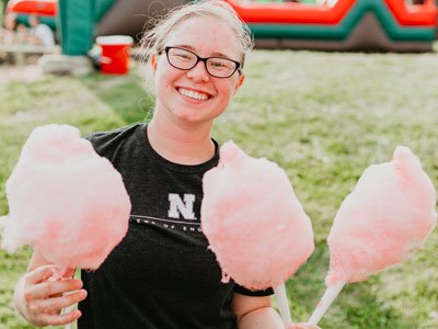 Smiling woman in black shirt holds three pink cotton candies on paper sticks