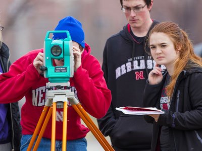 Three students standing outside with surveying equipment.