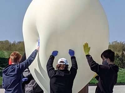 Students hold up a large white balloon used for testing a payload in space for a NASA competition