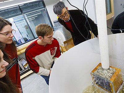 Students and a faculty member watch a bubbling fountain during an experiment.