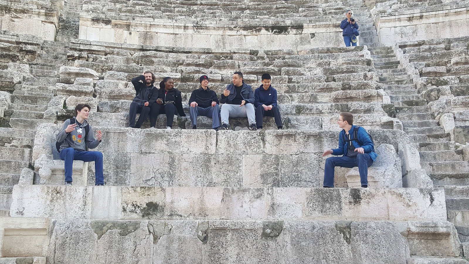 Group of students traveling abroad sitting on some ancient stone steps.